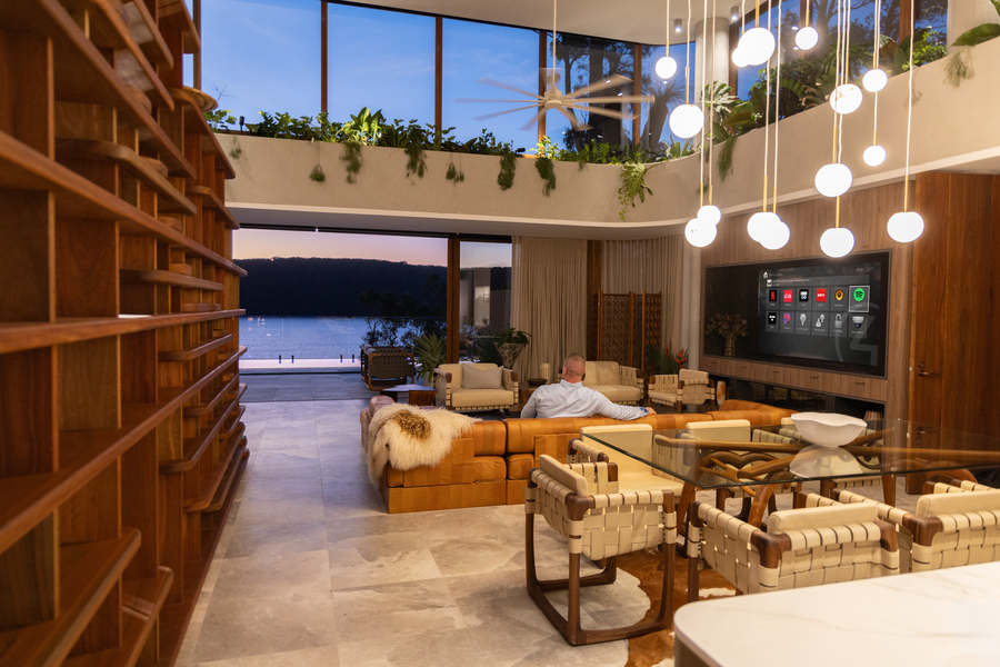 <p>Modern open-concept living room with smart home automation and large glass walls overlooking water</p>