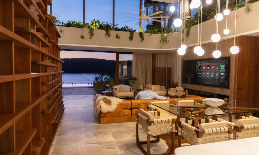 <p>Modern open-concept living room with smart home automation and large glass walls overlooking water</p>